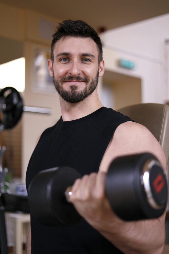 Confident male bodybuilder lifting a dumbbell indoors, showcasing strength and fitness.